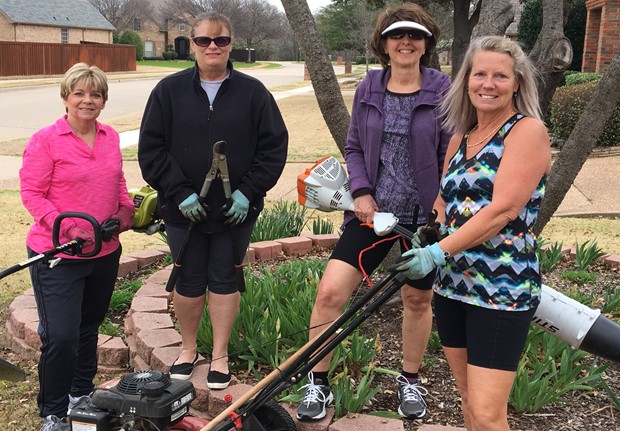 4 women standing in a yard with lawn tools